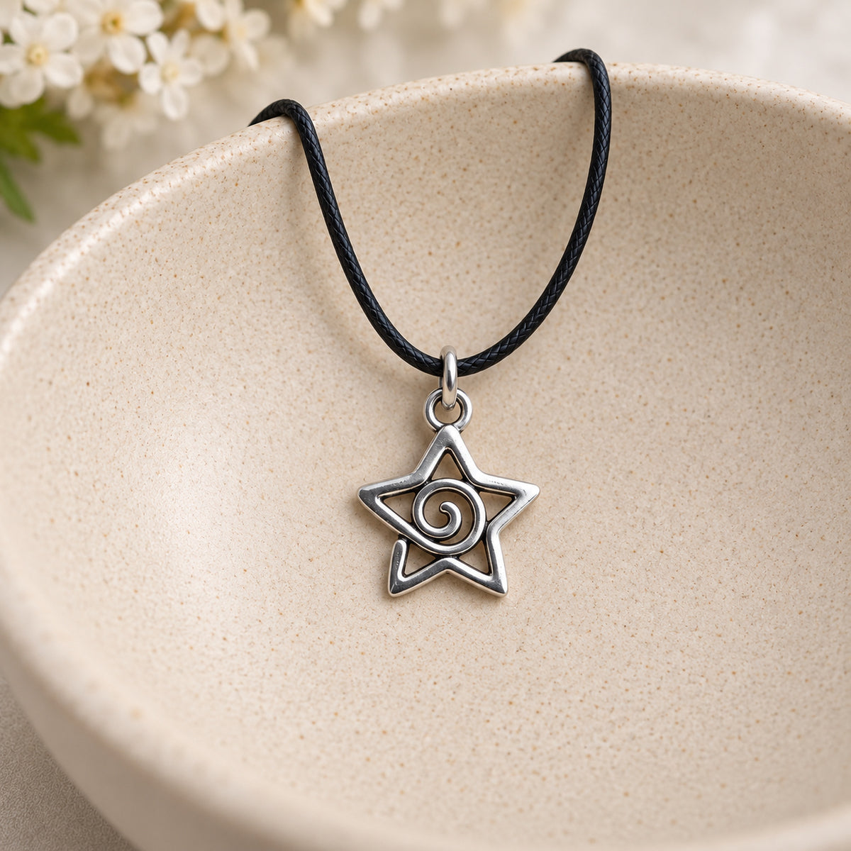 Silver-tone spiral star pendant on black cord resting in a speckled ceramic bowl
