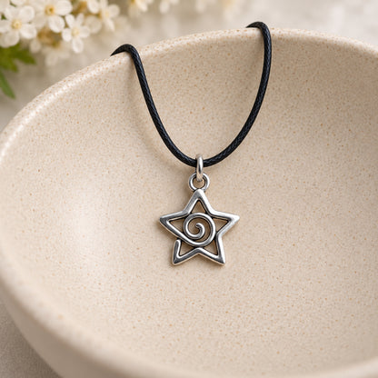 Silver-tone spiral star pendant on black cord resting in a speckled ceramic bowl