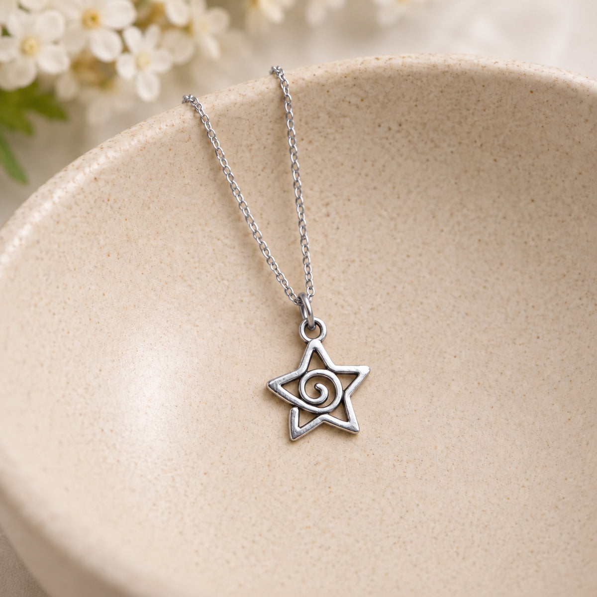 Silver-tone spiral star pendant and chain resting in a speckled ceramic bowl