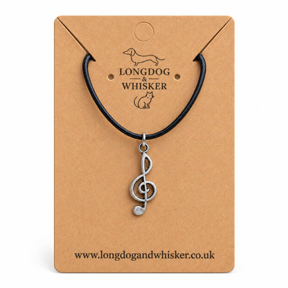 Silver-tone treble clef music note necklace on black cord on its kraft product card
