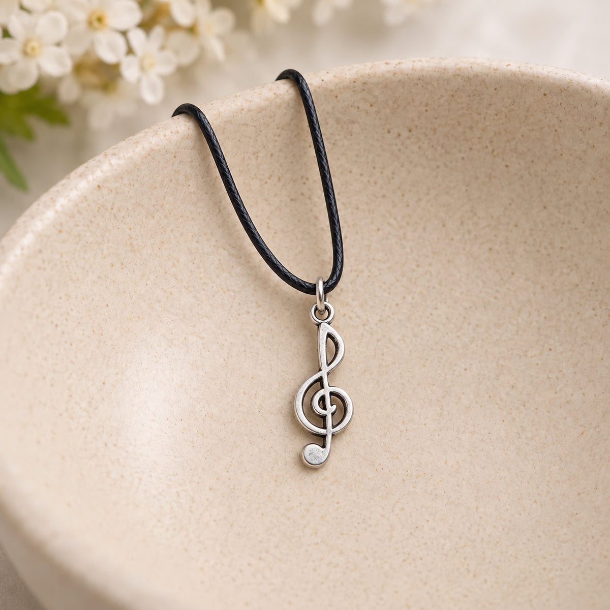 Treble clef pendant on black cord resting in a speckled ceramic bowl