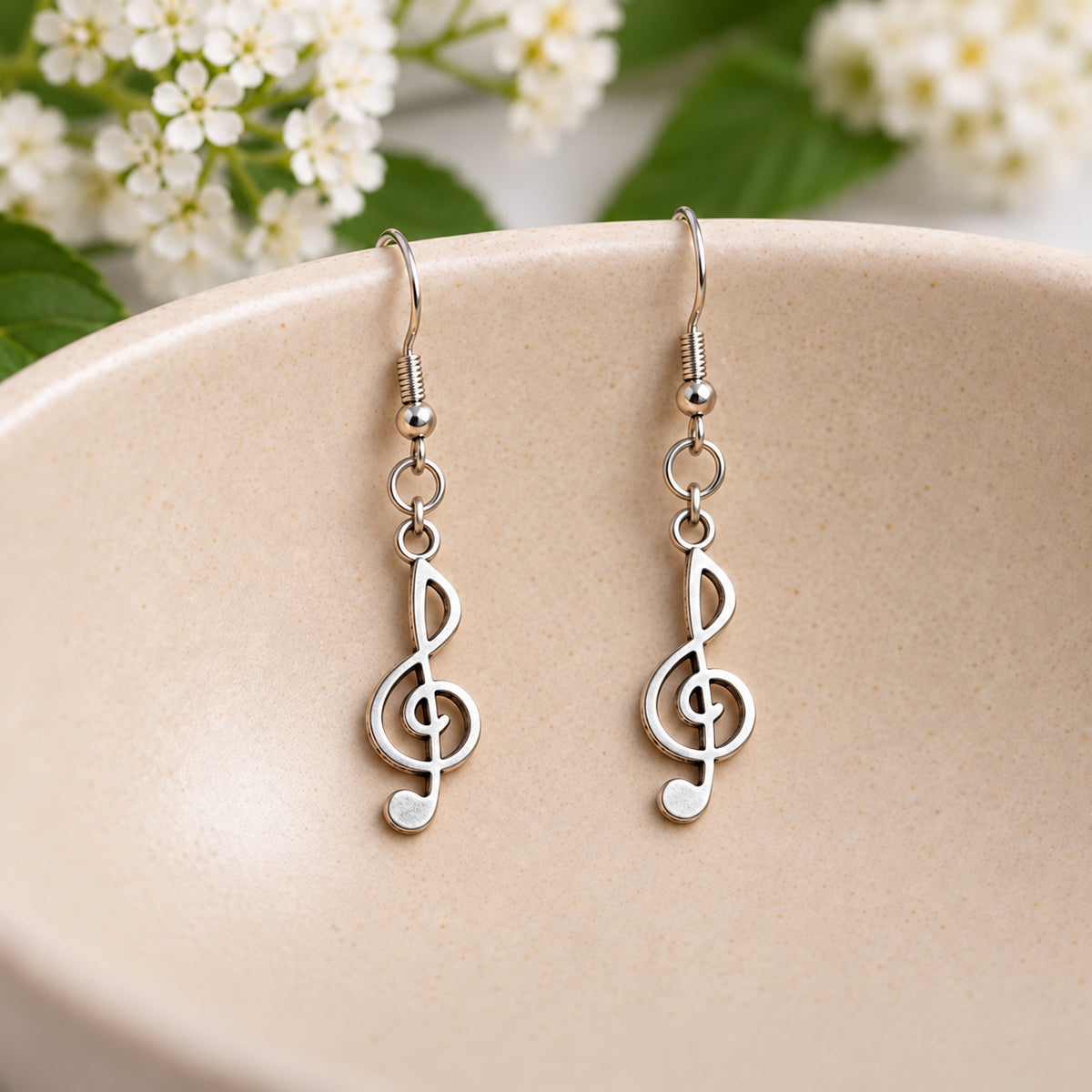 Silver-tone treble clef earrings hanging in a speckled ceramic bowl