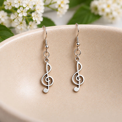 Silver-tone treble clef earrings hanging in a speckled ceramic bowl