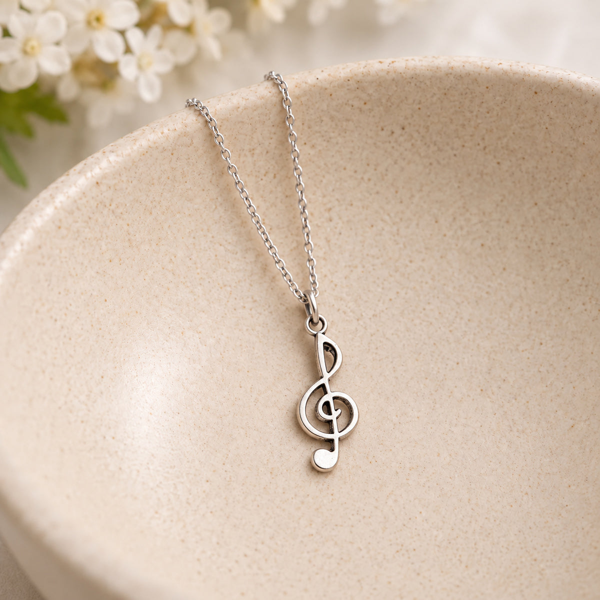 Silver-tone treble clef chain necklace resting in a speckled ceramic bowl
