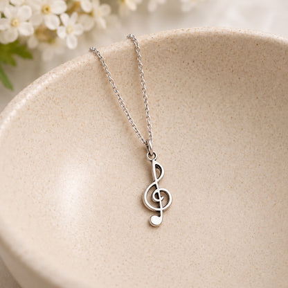 Silver-tone treble clef chain necklace resting in a speckled ceramic bowl