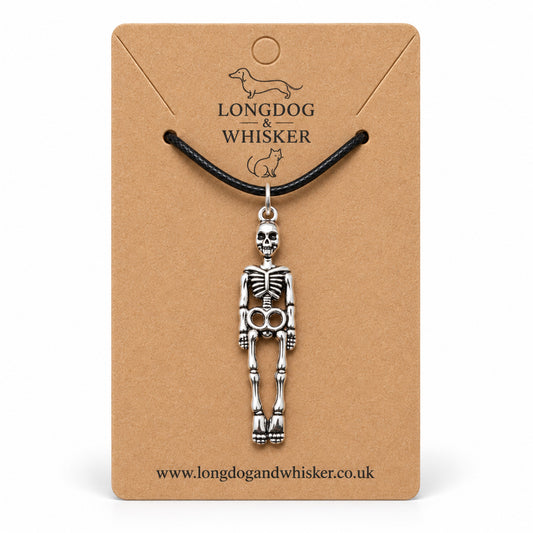 Silver-tone skeleton pendant on a black cord, displayed on a Longdog & Whisker kraft card