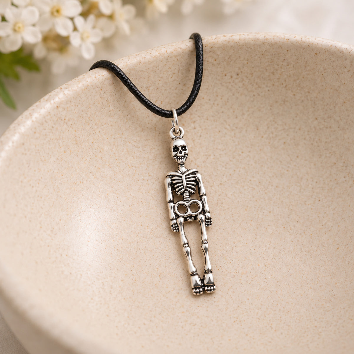 Skeleton black-cord necklace resting in a speckled ceramic bowl