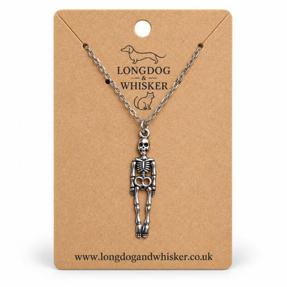 Silver-tone skeleton necklace on a silver chain, displayed on a Longdog & Whisker kraft card