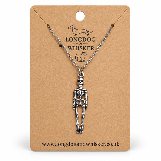 Silver-tone skeleton necklace on a silver chain, displayed on a Longdog & Whisker kraft card