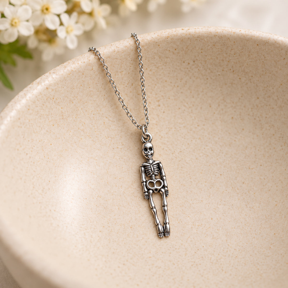 Silver-tone skeleton pendant and silver chain resting in a speckled ceramic bowl