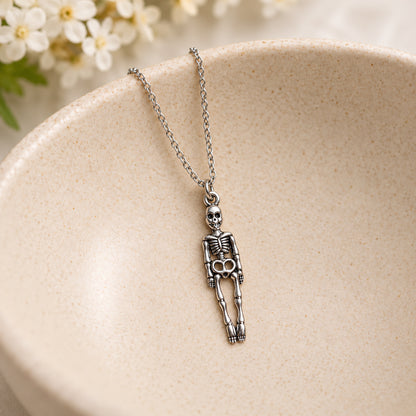 Silver-tone skeleton pendant and silver chain resting in a speckled ceramic bowl