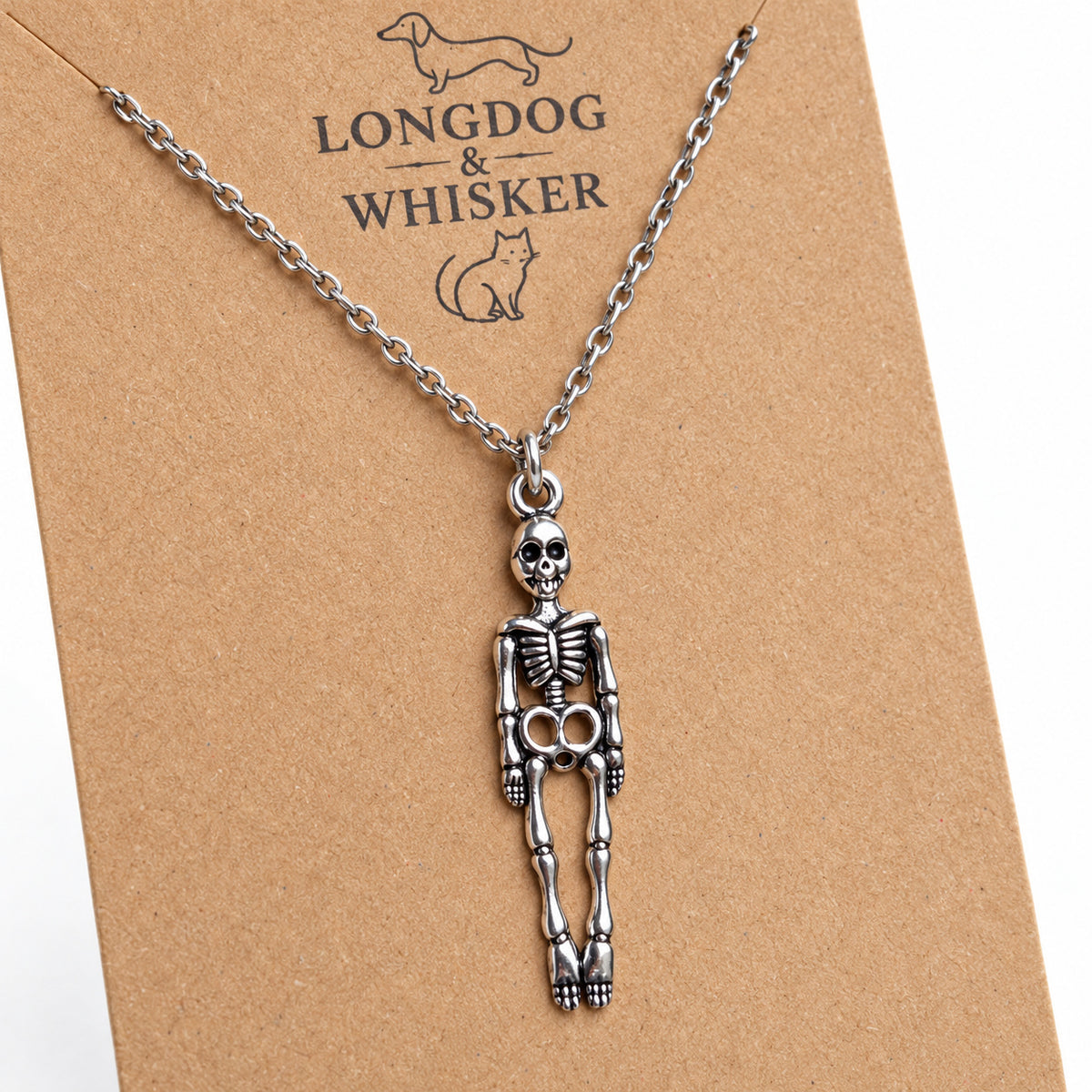 Close-up of the silver-tone skeleton pendant, connecting ring and silver chain on kraft card