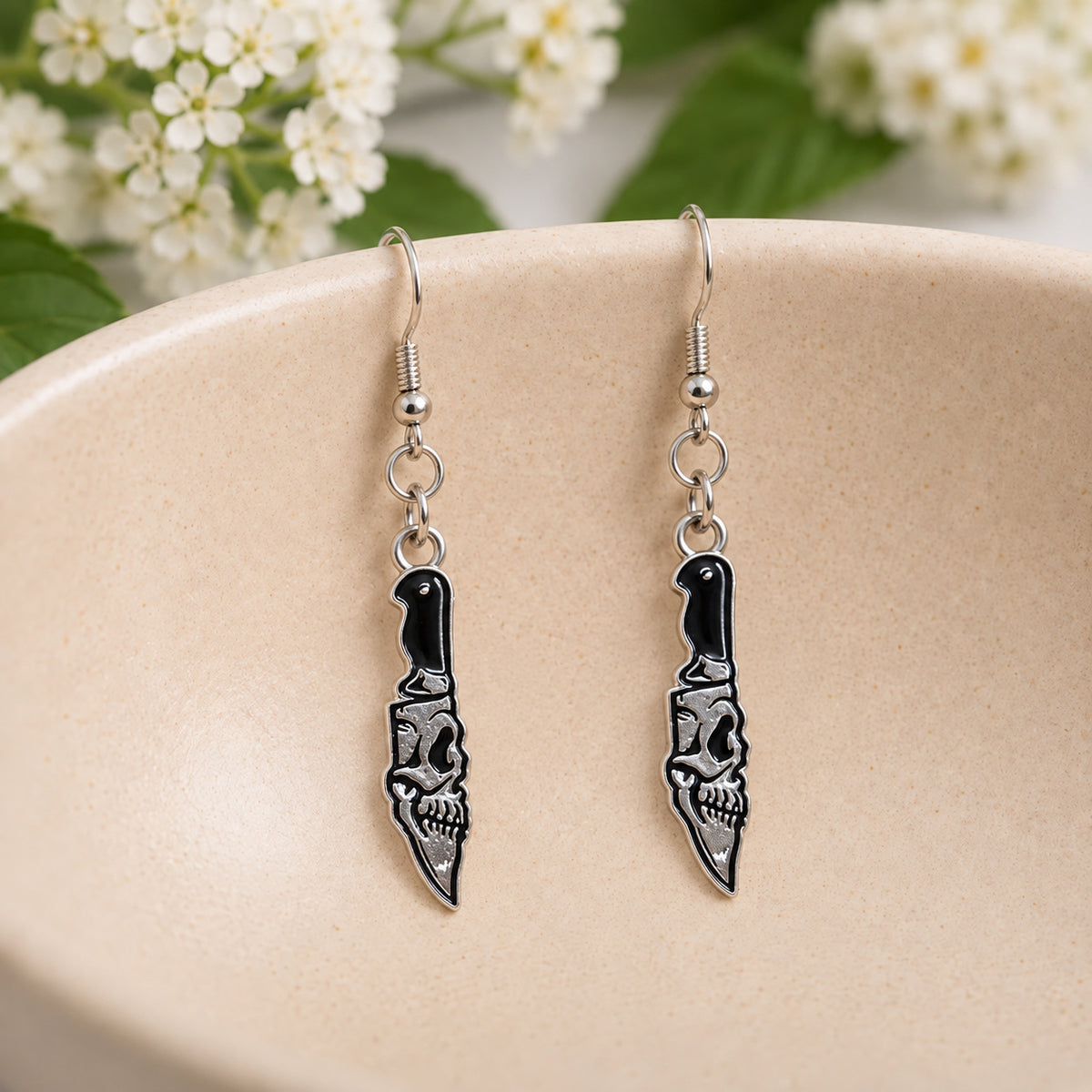 Black and silver-tone skull blade knife earrings in a styled lifestyle setting