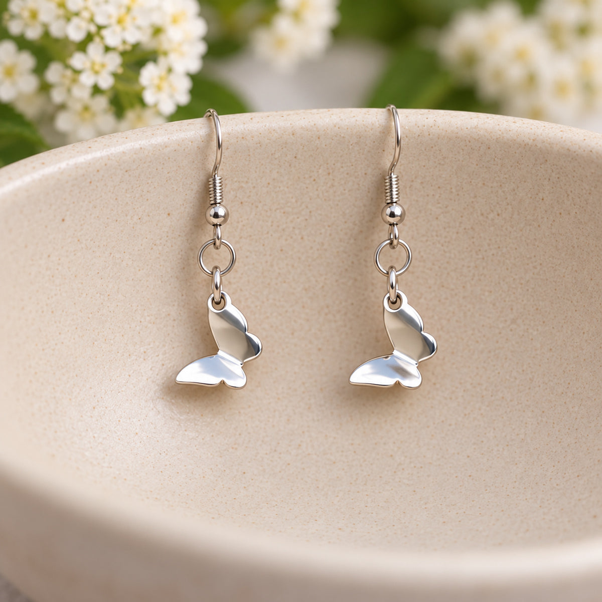 Polished stainless steel butterfly earrings hanging in a speckled ceramic bowl