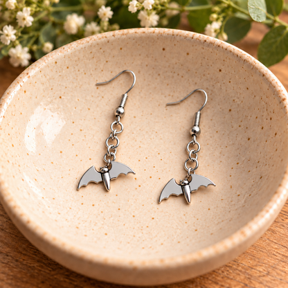 Stainless steel flying bat earrings displayed in a speckled ceramic bowl