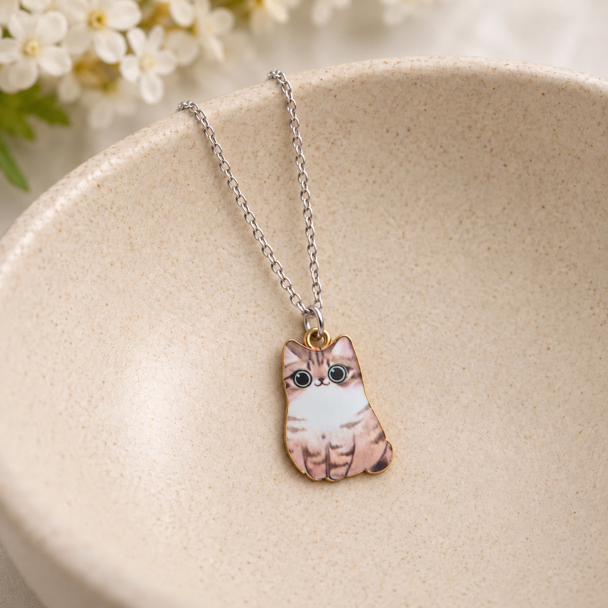 Brown tabby cat pendant with a white bib on a silver chain in a speckled ceramic bowl