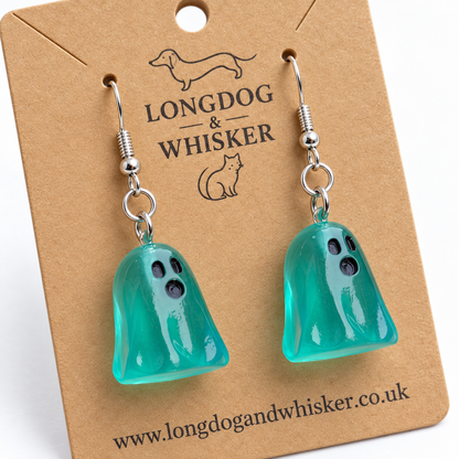 Close-up of aqua ghost earrings showing their glossy translucent finish, black faces and silver hooks.