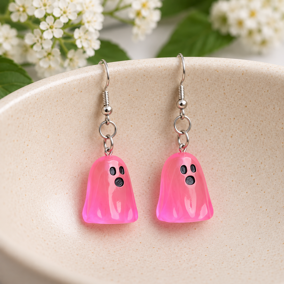 Translucent bright pink ghost earrings resting in a speckled ceramic bowl