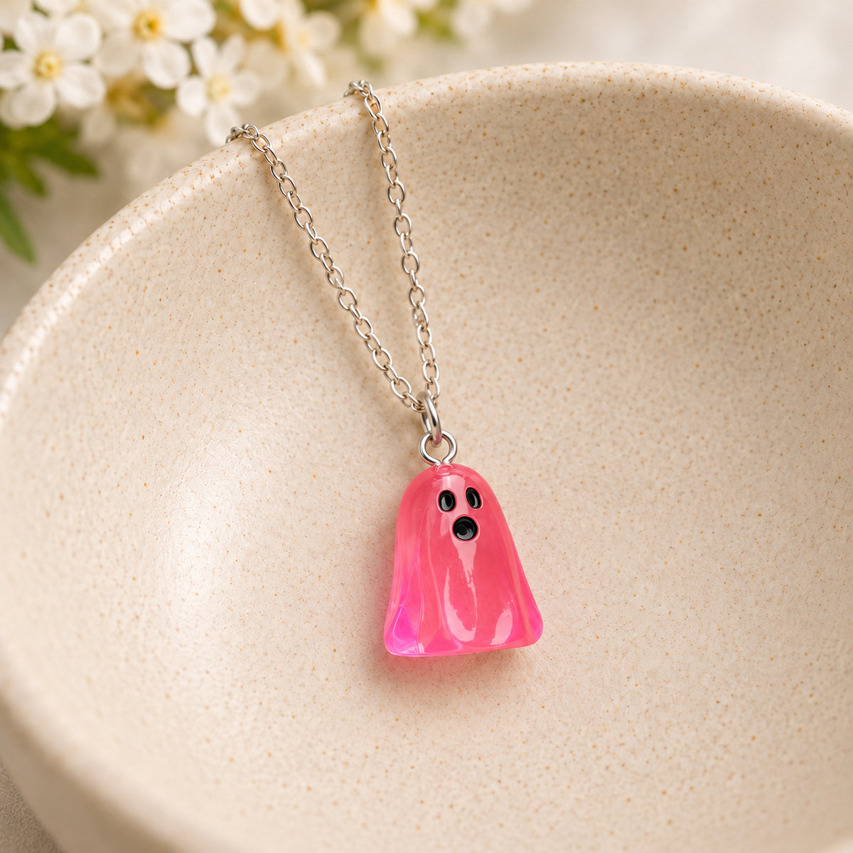 Translucent bright pink ghost necklace resting in a speckled ceramic bowl.