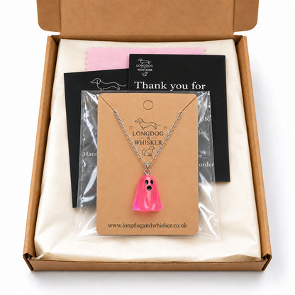 Translucent bright pink ghost necklace on its card in Longdog & Whisker postal packaging.