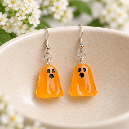 Translucent orange ghost earrings displayed in a cream ceramic bowl