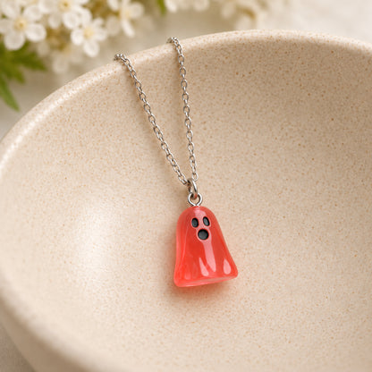 Translucent pale red ghost necklace resting in a speckled ceramic bowl.