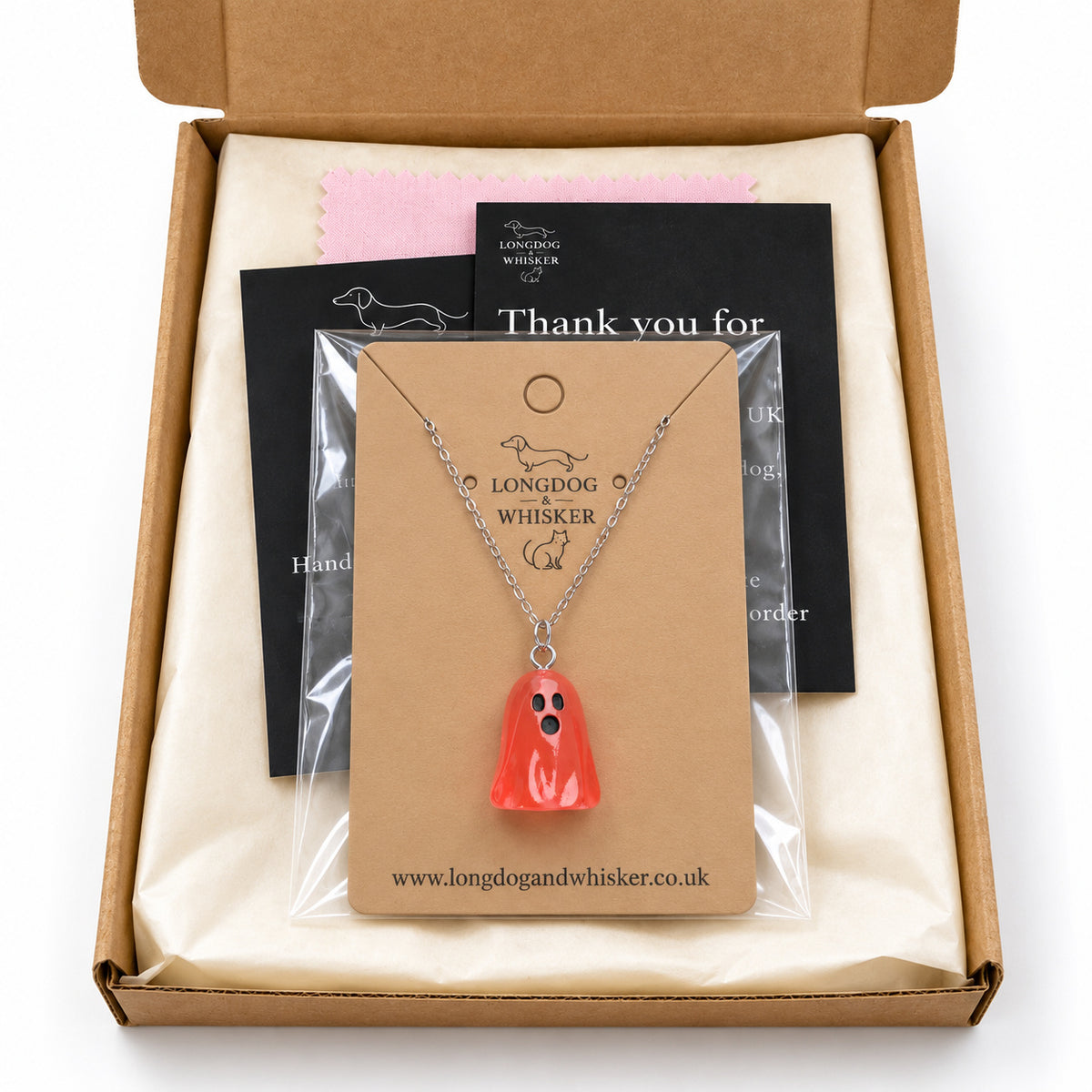 Translucent pale red ghost necklace on its card in Longdog & Whisker postal packaging.