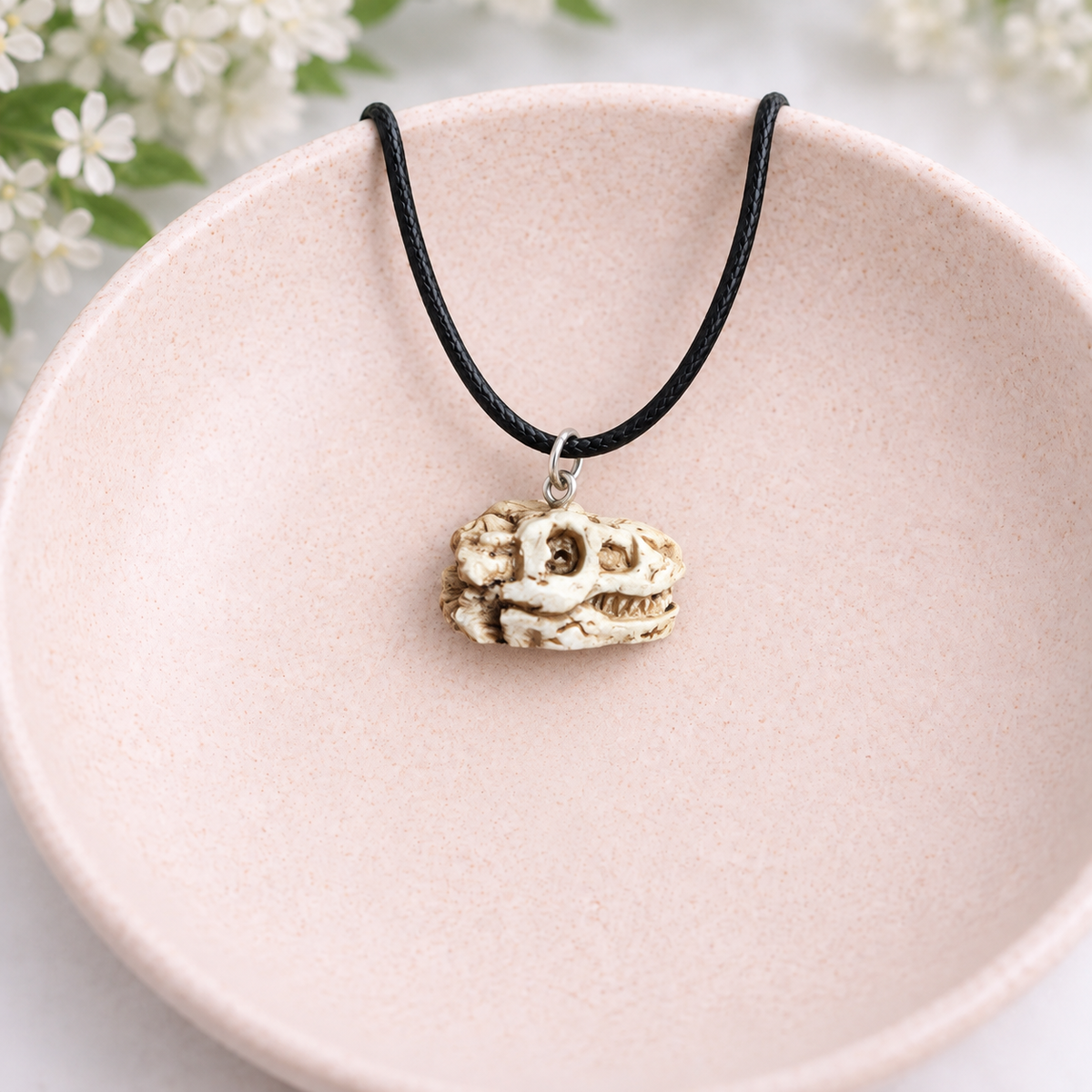 T-Rex dinosaur skull necklace displayed in a blush-pink speckled bowl