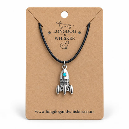 Silver-tone rocket necklace with turquoise porthole on black cord, displayed on a Longdog & Whisker kraft card