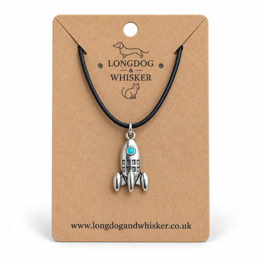 Silver-tone rocket necklace with turquoise porthole on black cord, displayed on a Longdog & Whisker kraft card