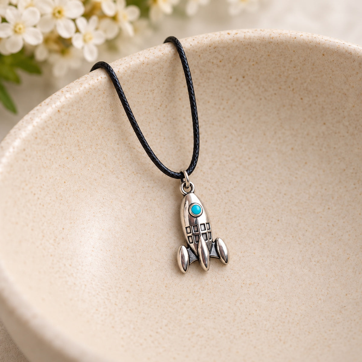 Turquoise porthole rocket necklace on black cord resting in a speckled ceramic jewellery bowl