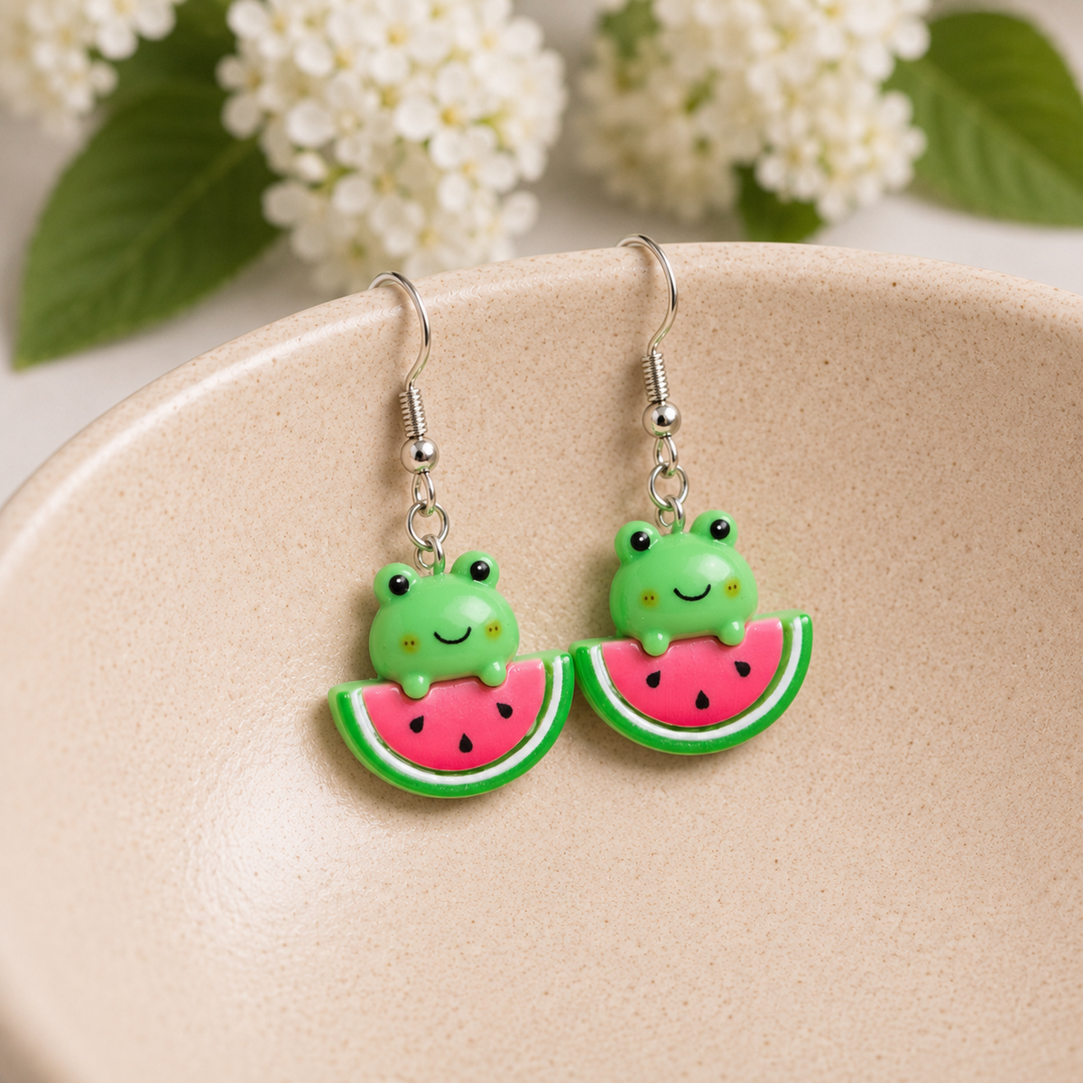 Watermelon Frog Earrings hanging over a ceramic bowl