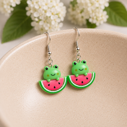 Watermelon Frog Earrings hanging over a ceramic bowl