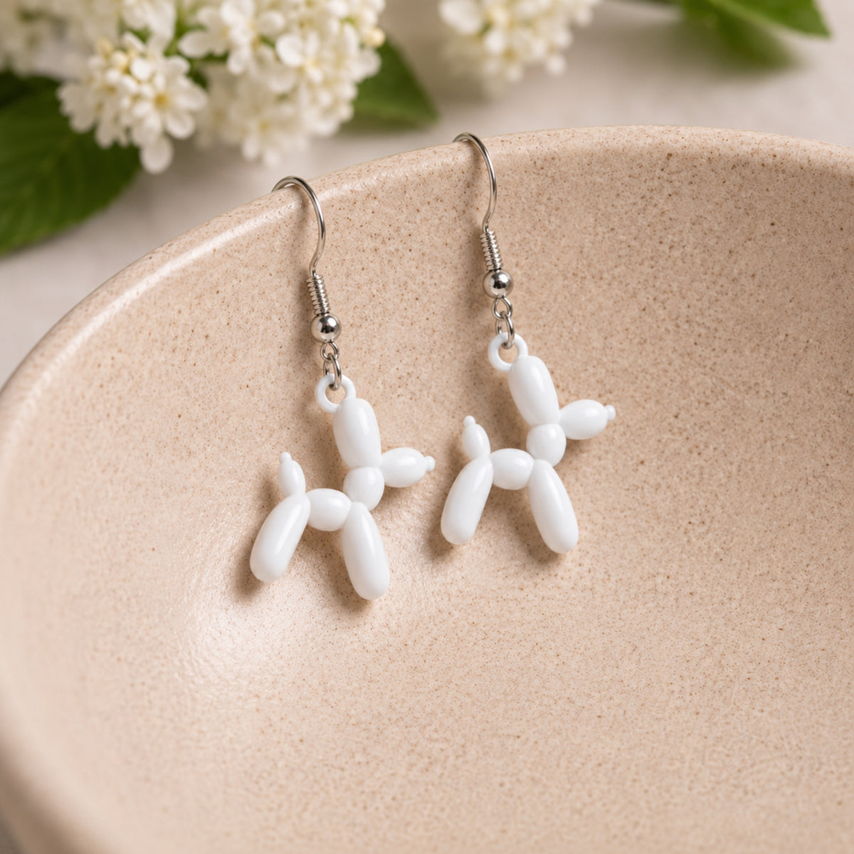 White Balloon Dog Earrings hanging from a ceramic bowl