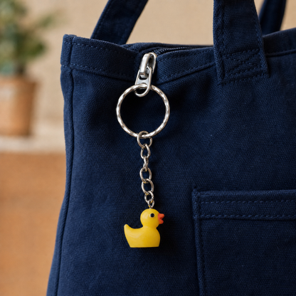 Yellow duck bag charm hanging from the zip of a navy blue canvas bag