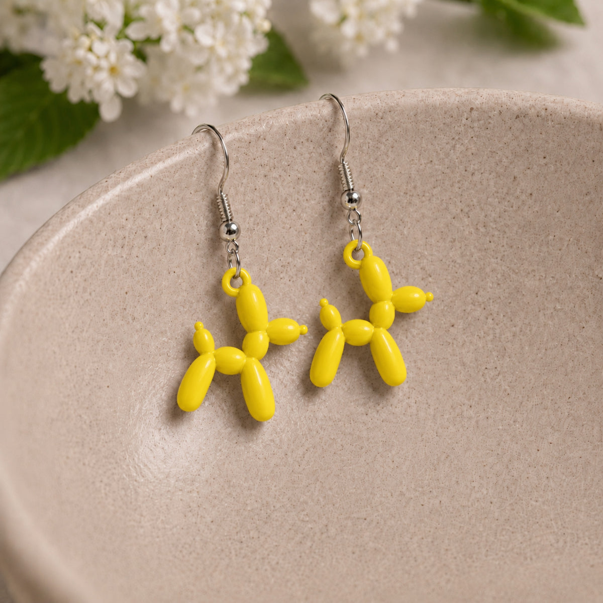 Yellow Balloon Dog Earrings hanging from a ceramic bowl