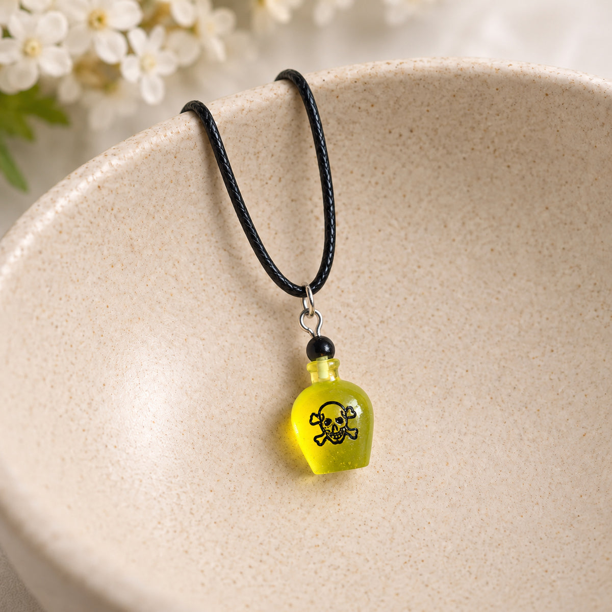 Yellow poison bottle necklace on black cord resting in a speckled ceramic bowl.