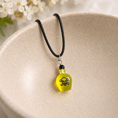 Yellow poison bottle necklace on black cord resting in a speckled ceramic bowl.